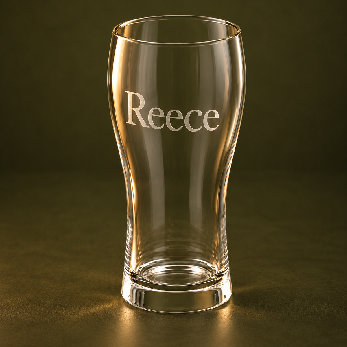 Close view of Reece engraved on a 570 ml beer glass against a dark olive backdrop